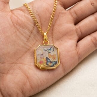 Handcrafted resin necklace featuring butterfly illustrations and a gold chain.