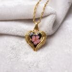Real pink flower set in a black resin heart with golden wings