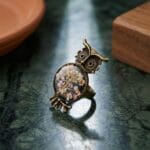 Close up of an owl resin ring with real dried wild flowers on a dark base