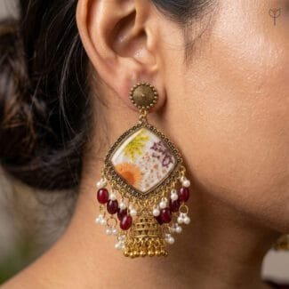 Model wearing the Gilded Lace Meadow Resin Jhumka, showing the diamond-shaped drop and maroon bead tassels.