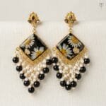Onyx Daisy Jhumka with pressed white daisies and baby's breath set in black resin, framed in golden metal.