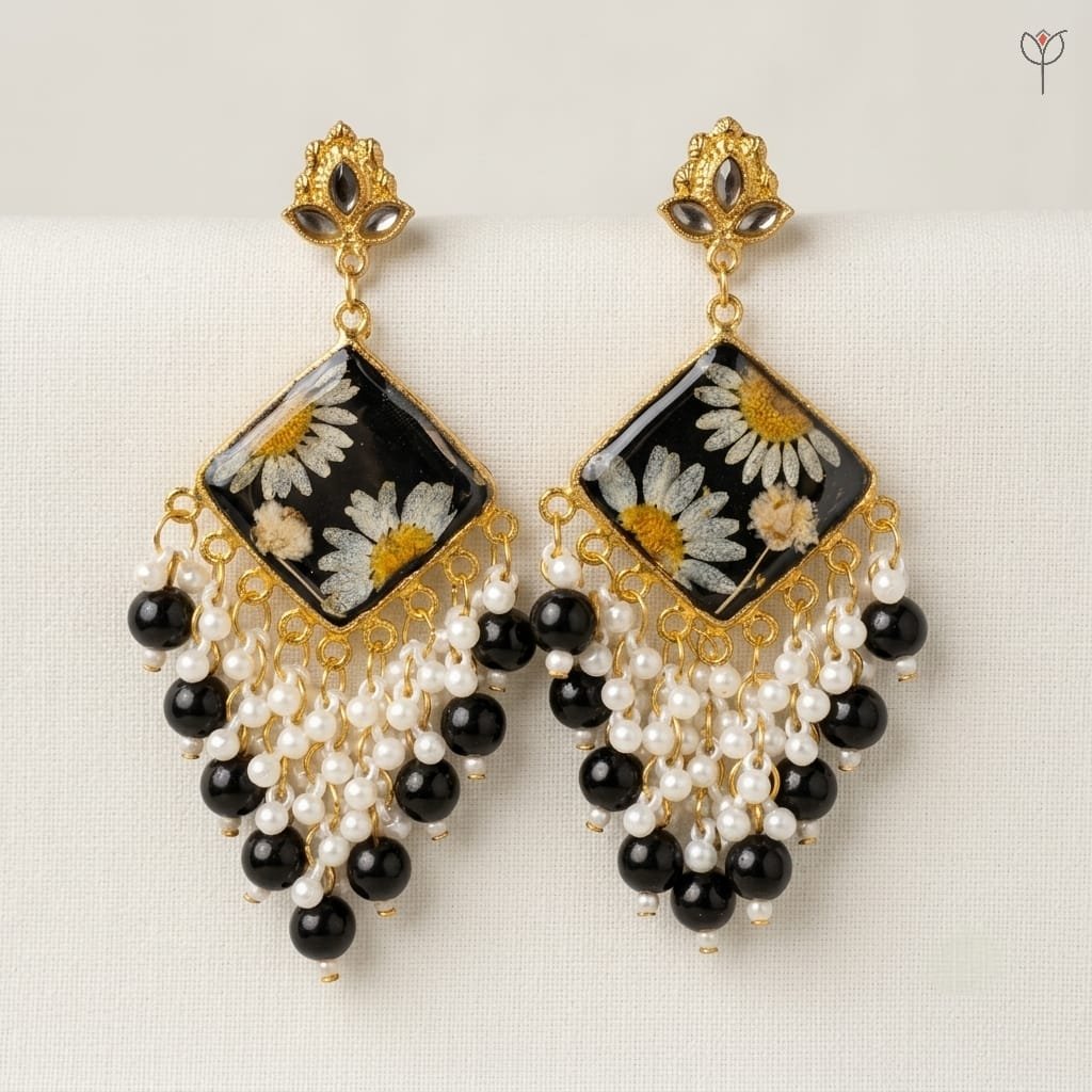 Onyx Daisy Jhumka with pressed white daisies and baby's breath set in black resin, framed in golden metal.