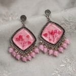 MystikFalls Pink Frost Jhumkas from a side angle – Showing pink resin depth with preserved baby's breath flowers, silver oxidised frame edge and pink bead dangle arrangement