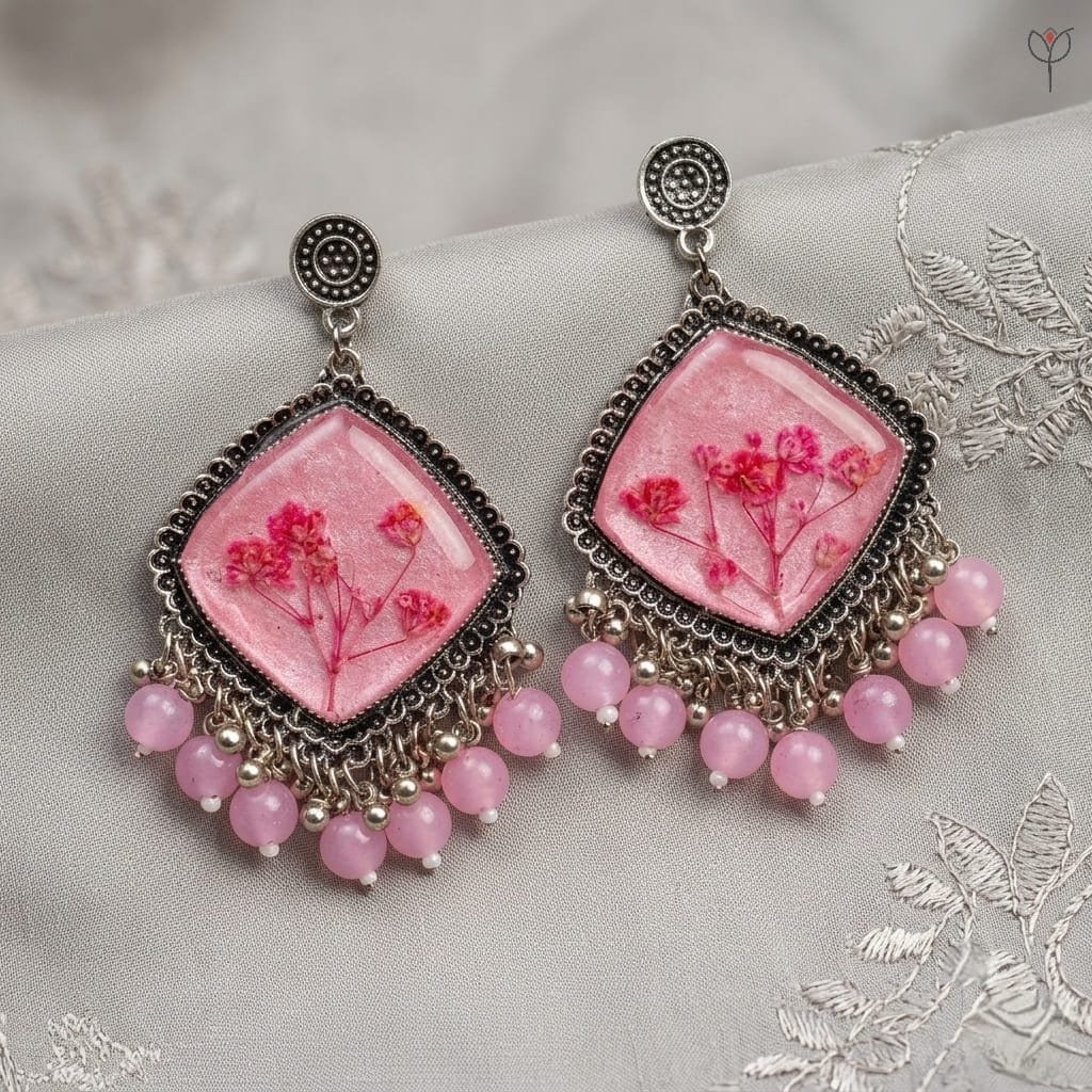 mystikfalls-pink-frost-jhumkas-styled-on-linen-with-dried-flowers MystikFalls Pink Frost Jhumkas from a side angle – Showing pink resin depth with preserved baby's breath flowers, silver oxidised frame edge and pink bead dangle arrangement
