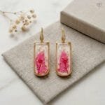 Liora Resin Earrings styled as handcrafted botanical drop jewellery with real preserved pink leaf in resin and gold-toned pavé ear hooks
