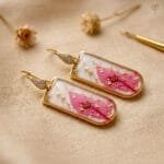 Liora Resin Earrings featuring preserved pink leaf with gold foil flakes in a rectangular golden frame with studded hooks by MystikFalls
