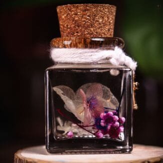 Secret Key Glass Garden close-up of real pink veined skeleton flower and purple hydrangea cluster in clear mineral oil